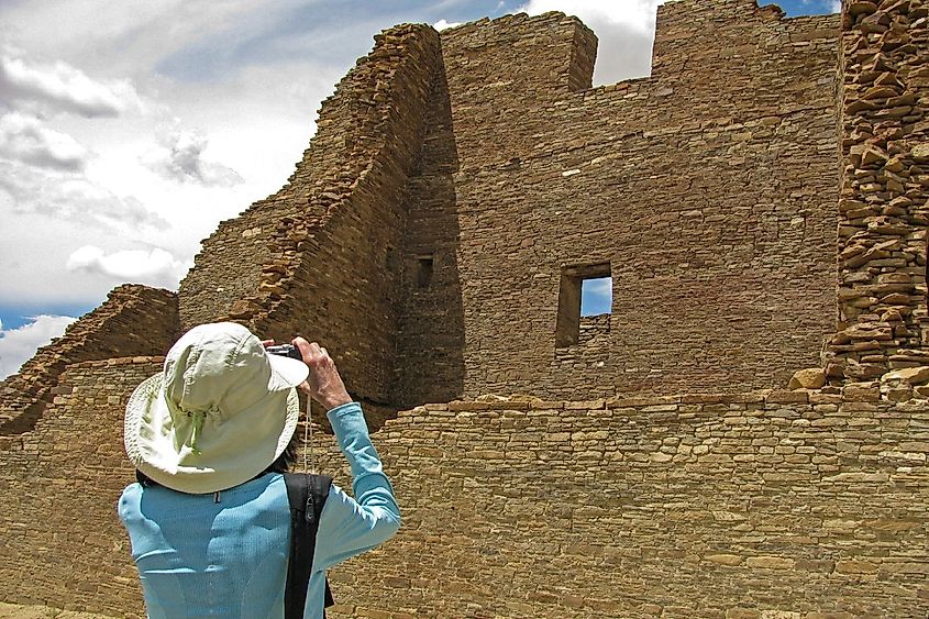 A female photographer shoots a photo of Pueblo Bonito Anasazi stone wall ruins in Chaco Canyon National Historical Park, New Mexico.