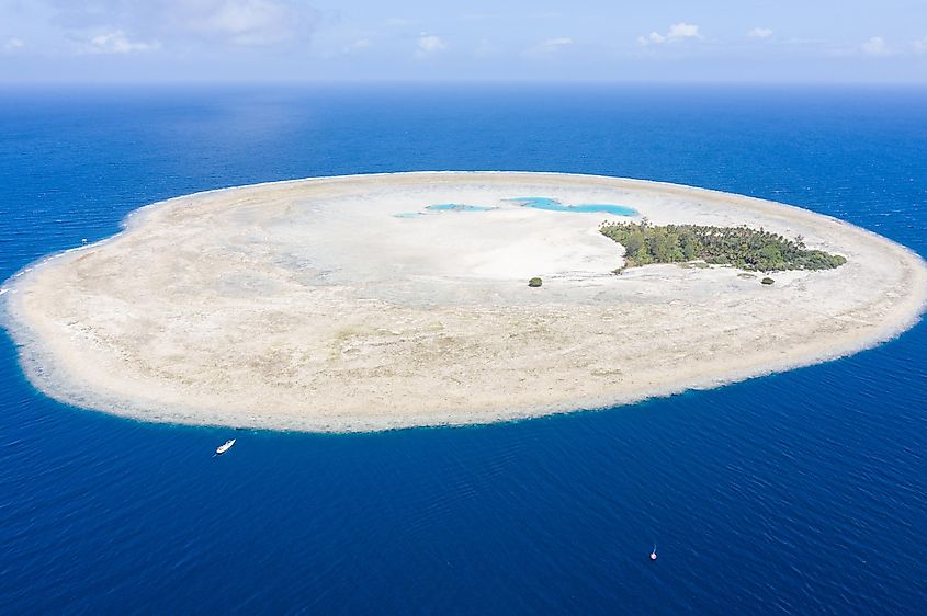 The idyllic island of Pulau Midorang is surrounded by a circular coral reef in the blue waters of the Ceram Sea, Indonesia.