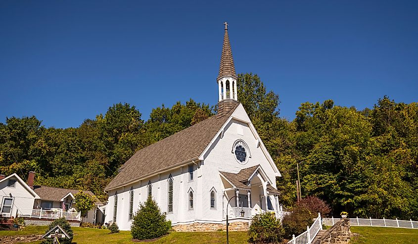 This image shows and idyllic rural, small town church chapel building with trees and a blue sky behind.