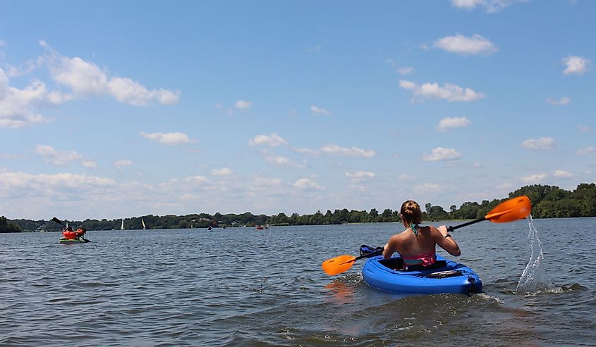 girl in kayak paddling on Lake MacBride Iowa on a sunny day with small puffy clouds in clear blue sky on calm waters.