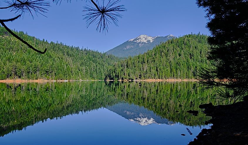 Waters of Trinity Lake are perfectly calm allowing a mirror-image reflection of snow-capped mountains in the Trinity Alps range, Northern California