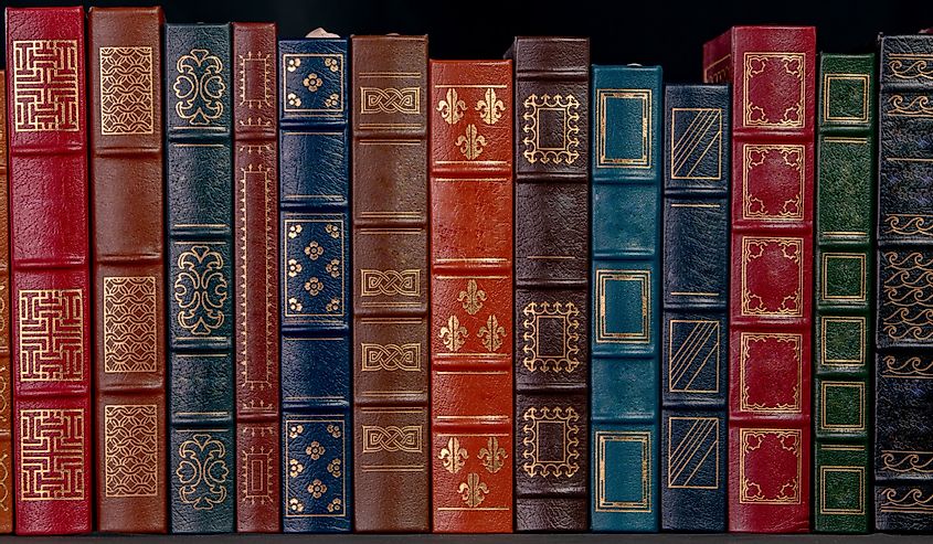 A stack of beautiful leather bound books with golden decoration against a black background.