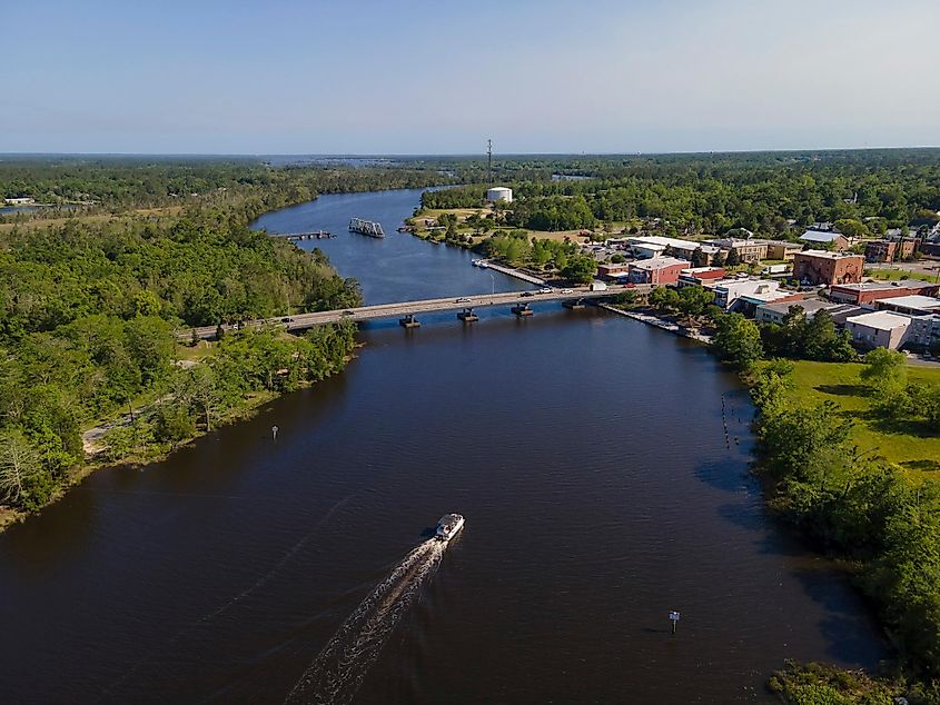 Passenger boat traveling under bridges on a wide river in Milton, Florida. Land areas with trees on the left and buildings on the right connected by the bridges.