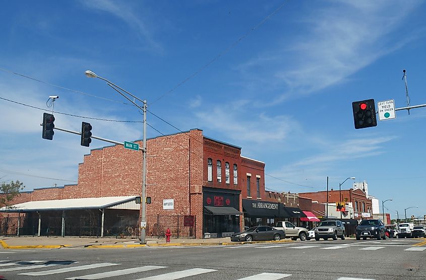 Main street with red brick buildings in Yukon, Oklahoma with cars stopping for a red light, via Raksybh / shutterstock