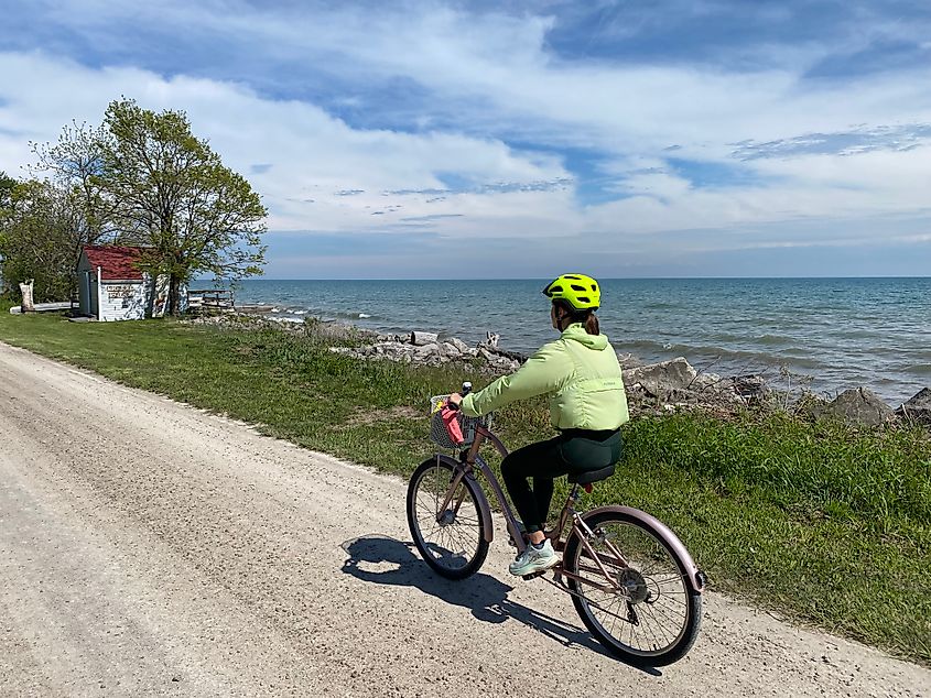 A woman in all green rides a cruiser bike on a waterfront gravel road.