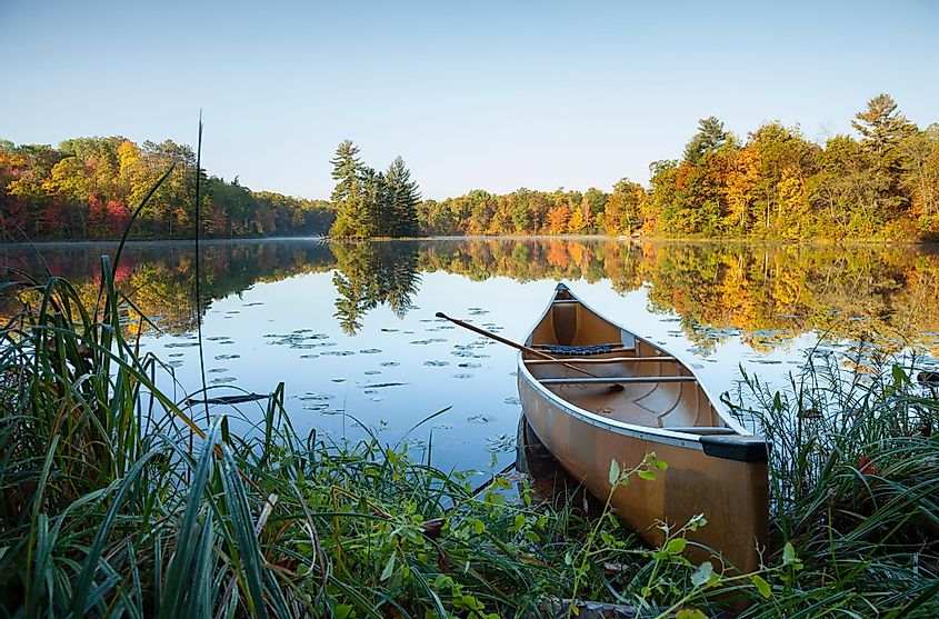 Canoe with paddle on shore of beautiful lake with island in northern Minnesota at sunrise.