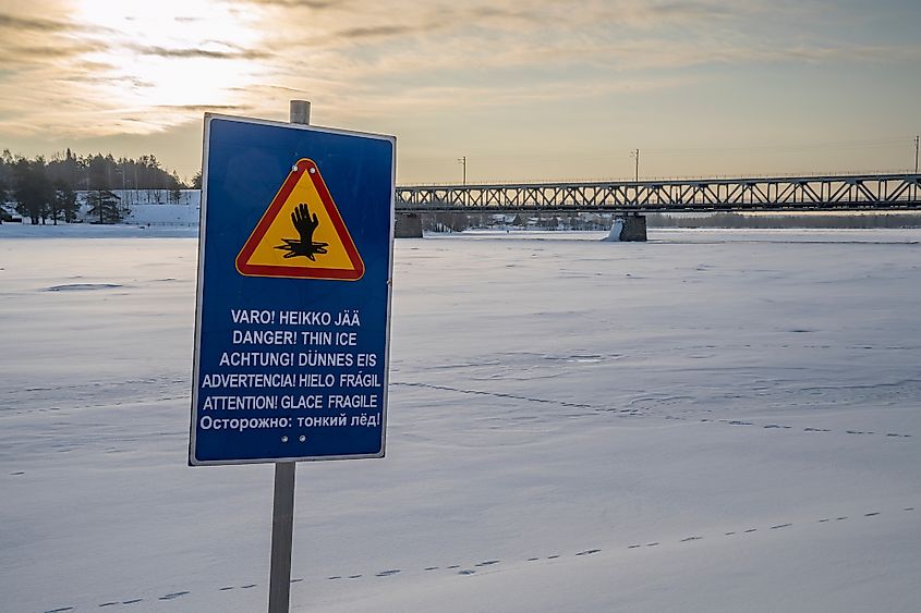 A "thin ice" multilingual warning sign on the bank of the frozen Kemijoki river, Rovaniemi, Finland.