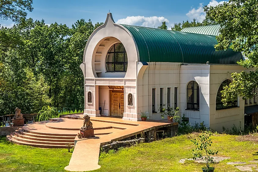 The New Temple at the Peace Pagoda in Leverett, Massachusetts, with arched windows, a green domed roof, and lion statues set against a forest backdrop