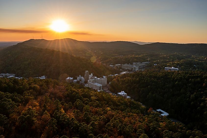 The evening sun sinks towards the horizon over the Ouachita Mountains surrounding the historic downtown of Hot Springs, Arkansas, during autumn.