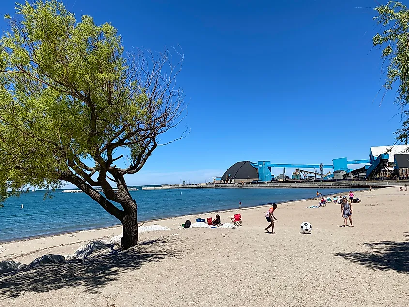 People kicking a large soccer ball on a sandy lake beach. 