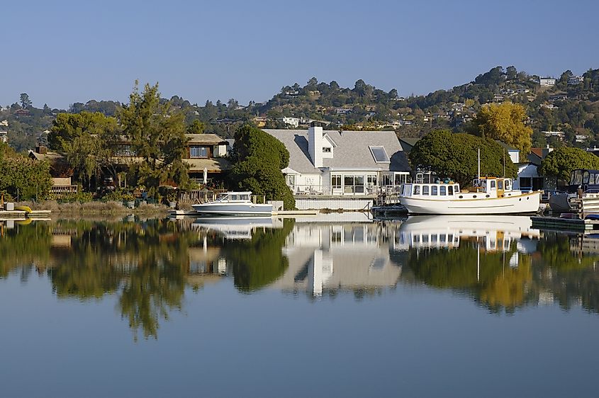 Nice houses with boats are reflected in calm waters of Corte Madera Creek in Larkspur, California.