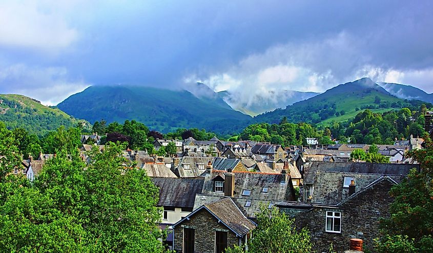 Looking over the roof tops of the town of Ambleside with green trees towards the start of a mountain range