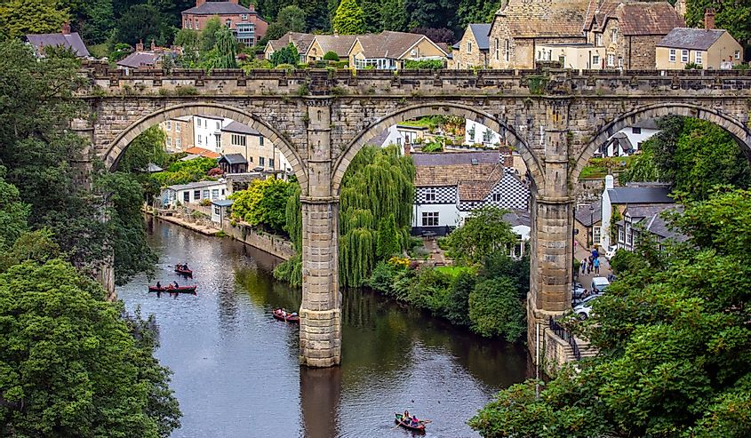 A beautiful view of Knaresborough Viaduct over the River Nidd in the town of Knaresborough in Yorkshire, UK with lush greenery and people in canoes on the water.