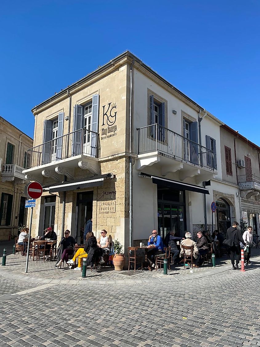 A busy bakery has full tables all around it's stone sidewalk/streets