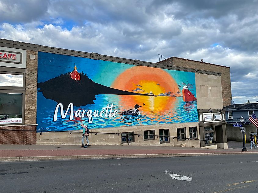A skateboarder glides past the colorful town mural for Marquette, Michigan