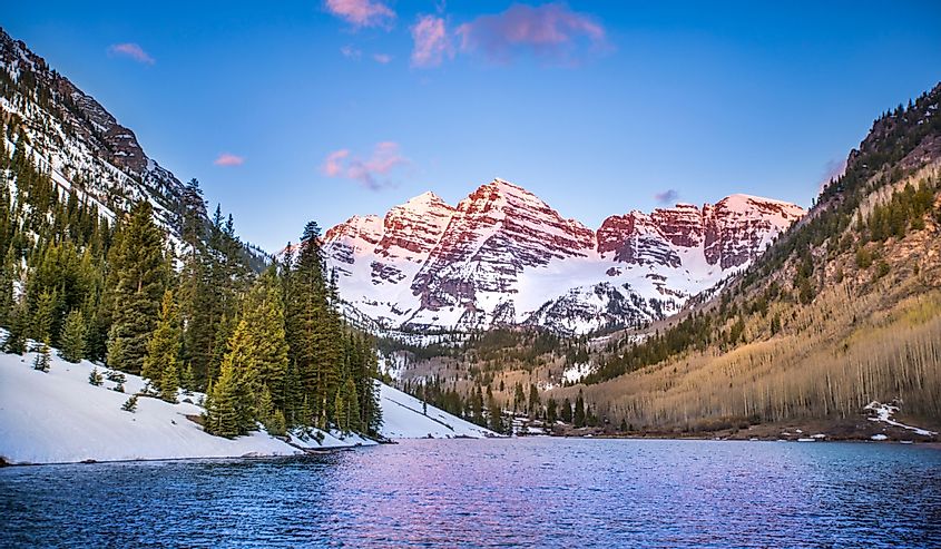 The Rocky Mountains near Aspen, Colorado glow in the light of the morning sunrise, as the mountains and trees reflect off the lake.