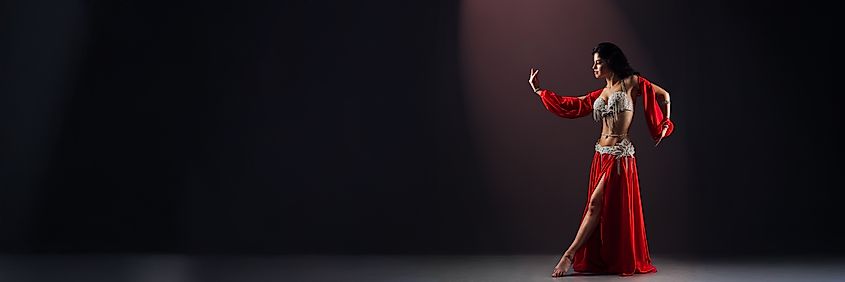 Expressionful belly dancer in vibrant red costume against dark background.