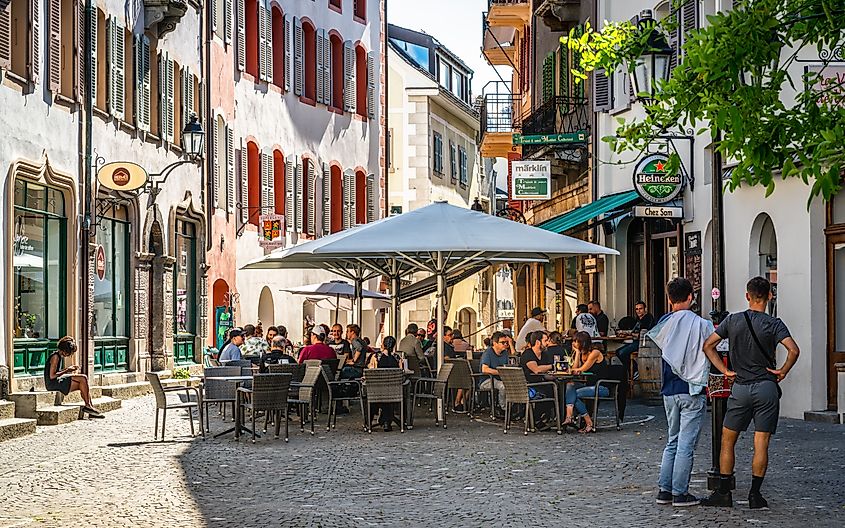 Bar terrace full of people on sunny summer day in pedestrian street of Sion old town Switzerland.