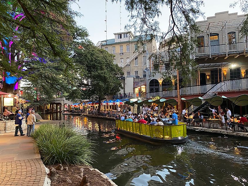 A boat full of tourists cruises along downtown San Antonio's colorful Riverwalk
