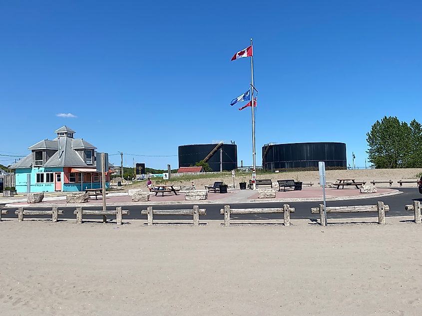 Two large black industrial facilities stand behind a beach and its defunct ice cream shack.