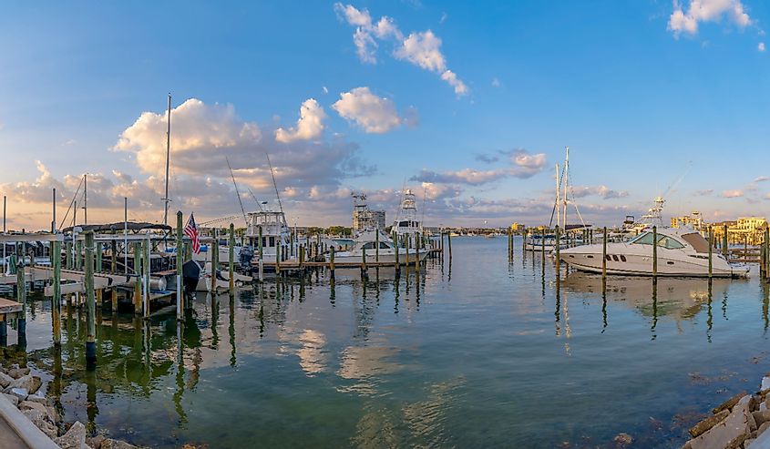 Boats anchored in the water of Destin Harbor. Scenic view of a boatyard with clear water reflecting the clouds and sky at sunset.