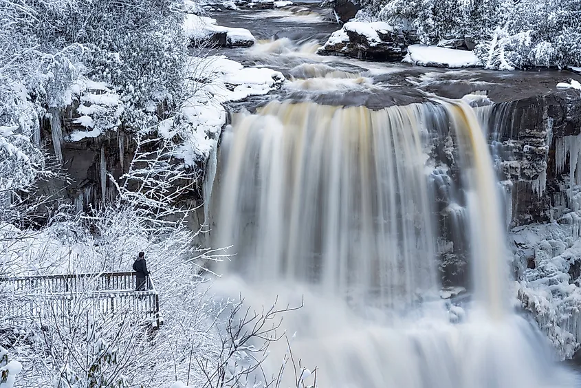 A man poses on viewing platform in front of Blackwater Falls on a winter day in Davis, West Virginia.