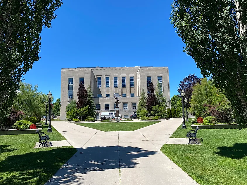 A boxy grey courthouse building stands at the center of a green, well manicured park. 