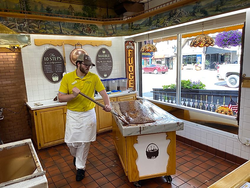 A man mixes a marble table of fudge within a Bavarian themed tourist shop. 