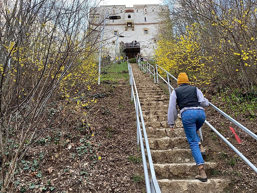 A woman in an orange toque walks a steep flight of stone steps up to an old white watchtower.