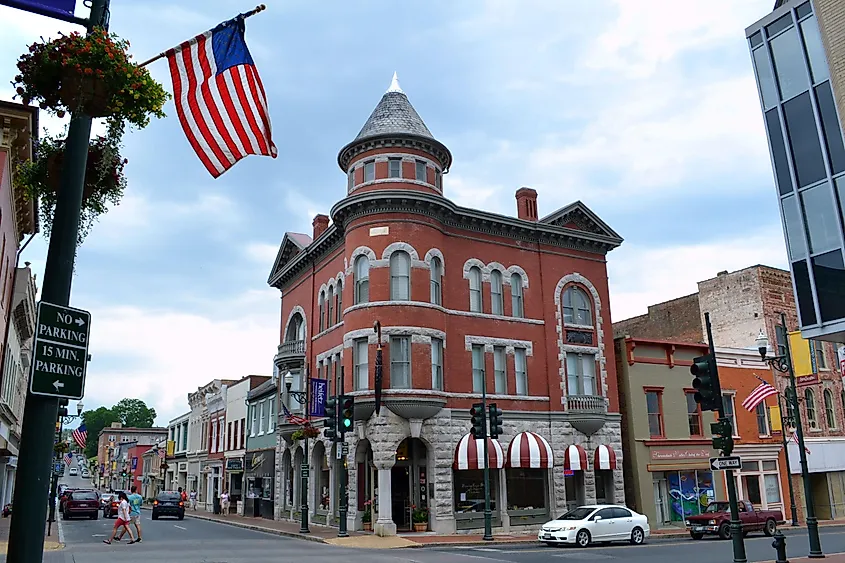Historic red brick building with ornate arches and turret on a small-town street. American flag waves, conveying a charming, nostalgic feel.