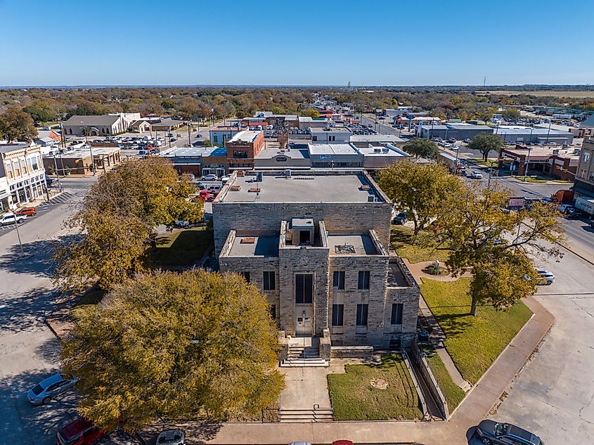 Aerial Drone View of Tall Old Stone Brick City Hall Building Entrance Surrounded By Trees in Comanche, Texas