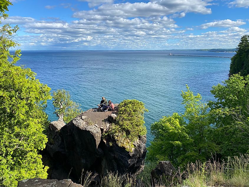 A hiking couple sits atop a rock pillar high above the waters of Lake Superior.