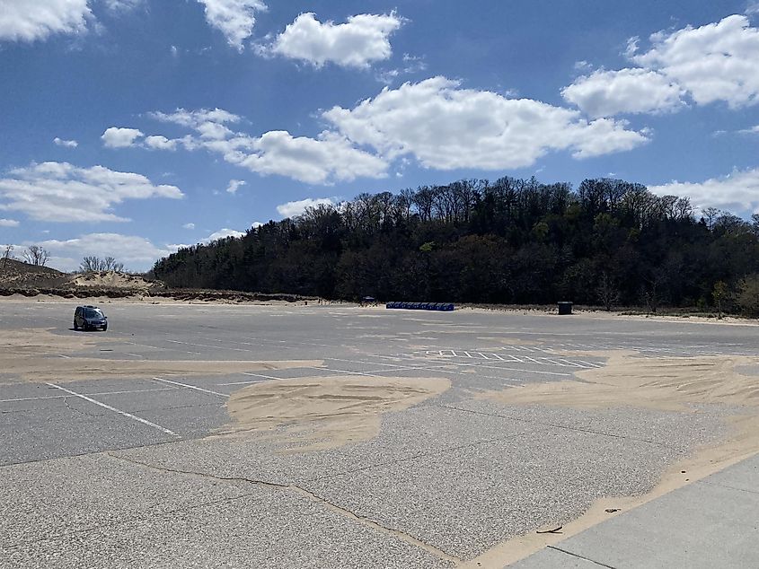 A small blue van sits alone in a large beach parking lot