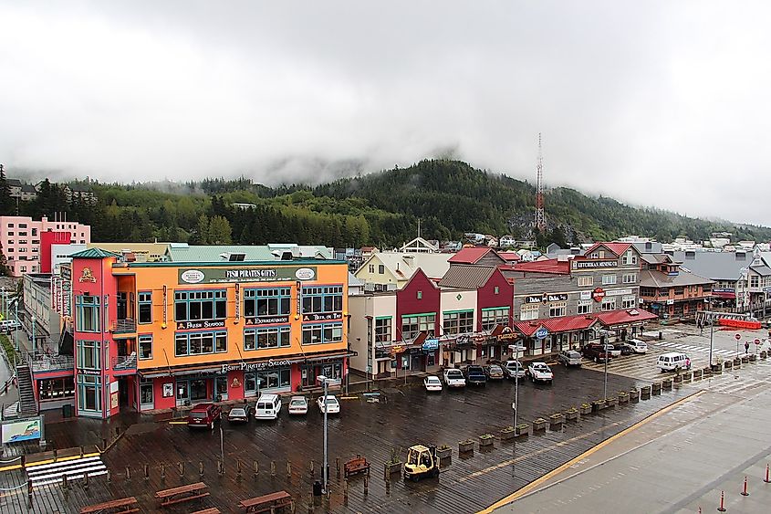 A row of colorful buildings in downtown Ketchikan with dense forest in the background and misty skies.