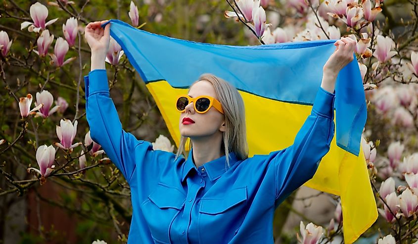 Woman in sunglasses and blue shirt with Ukranian flag near magnolia tree