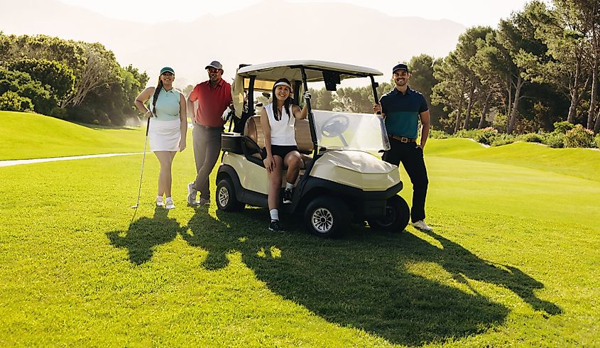 Men and women golfers posing together with a golf cart and clubs, symbolizing teamwork and friendship on a sunny golf course.
