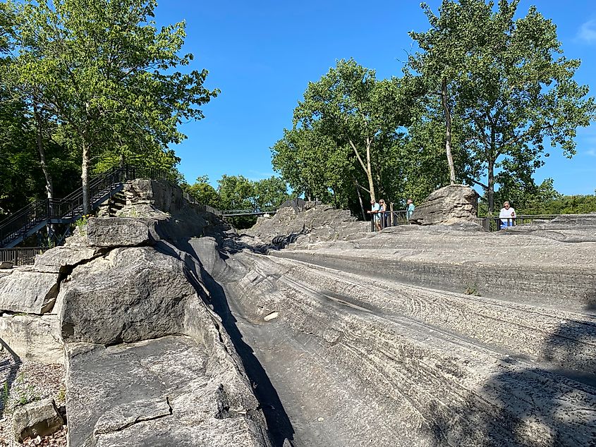 People standing on a viewing platform, overlooking long grooves in a rock slab. 