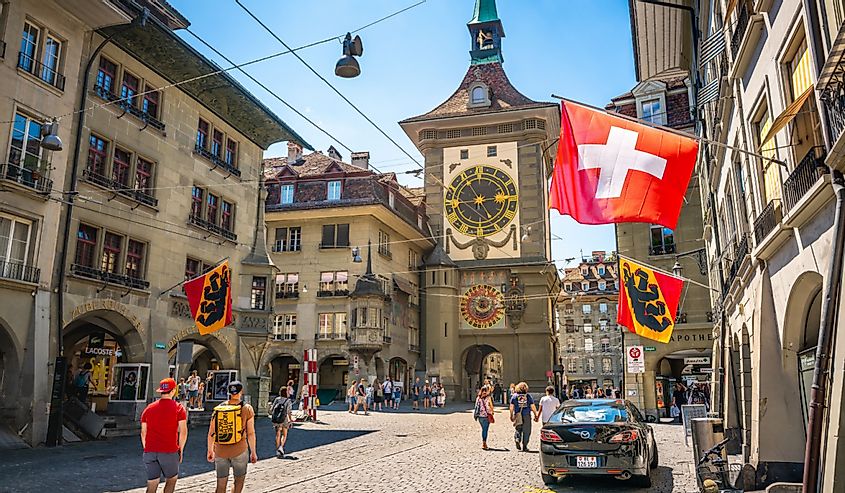 Old street view with tourists flags and Zytglogge clock tower in Kramgasse street in Bern old town Switzerland