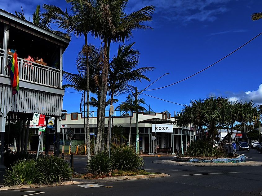 Horizontal photo of a roundabout, road, shops, a restaurant and tropical gardens edging the street at popular travel destination, Byron Bay on the north coast of New South Wales