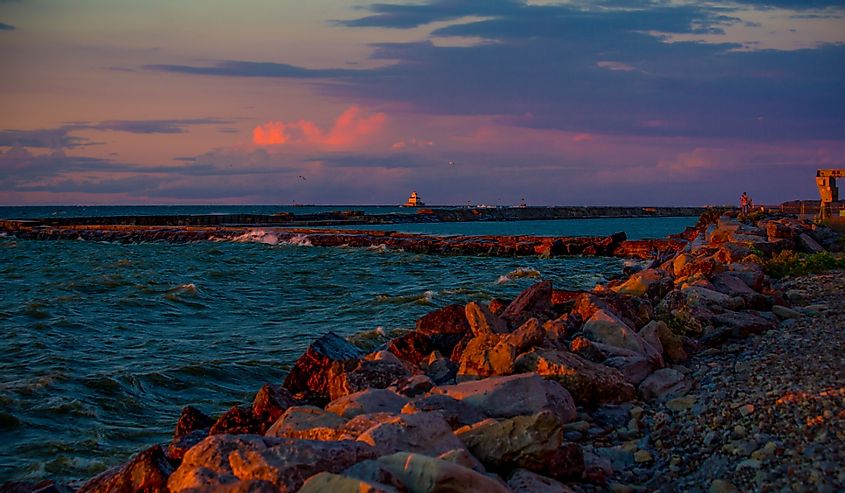 Sunset over Oswego Lighthouse in the distance with pink and red sky and wavy waters