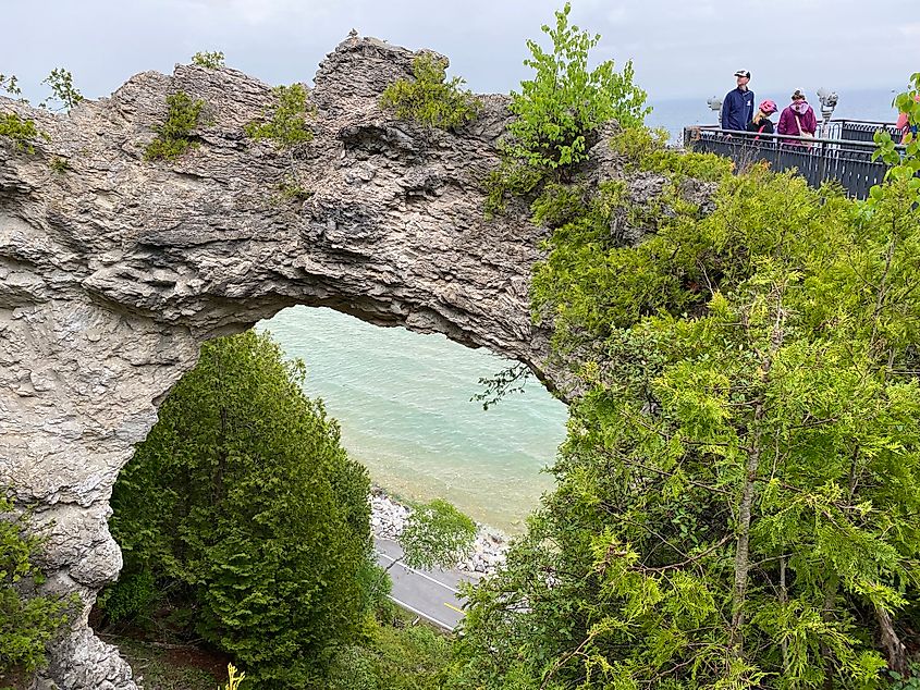 A family stands atop a lookout platform beside Arch Rock on Mackinac Island. The perimeter cycling road can be seen through the gap.
