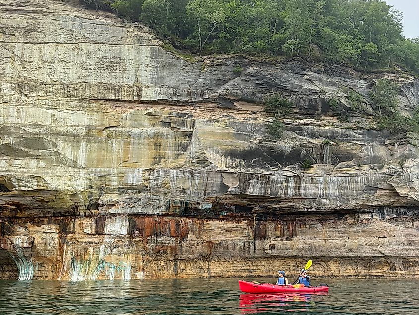 A couple of tandem kayakers paddle past the large colorful cliffs of Michigan's Pictured Rocks