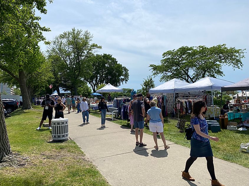 Crowds gathering amongst the antique dealers set up in tents beside a park path. 