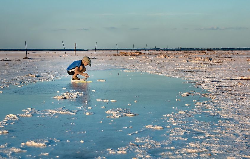 A young boy collects salt crystals in salt-saturated water. Salt Plains National Wildlife Refuge, Oklahoma, US.