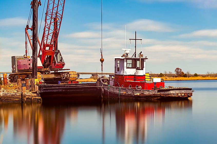 A small rustic vintage tow boat with chipped paint docked by a crane on Nanticoke river. 