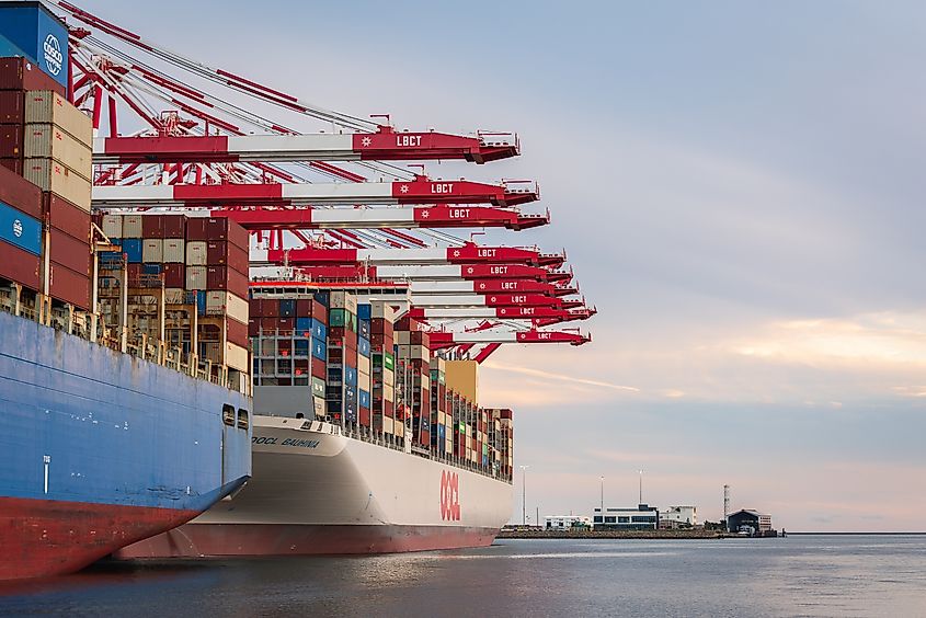 Container ships alongside red LBCT cranes at Port of Long Beach with stacked cargo and pastel sky