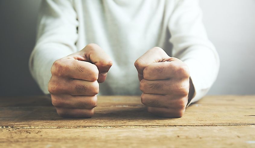 man fists clenched on a wooden table in anger