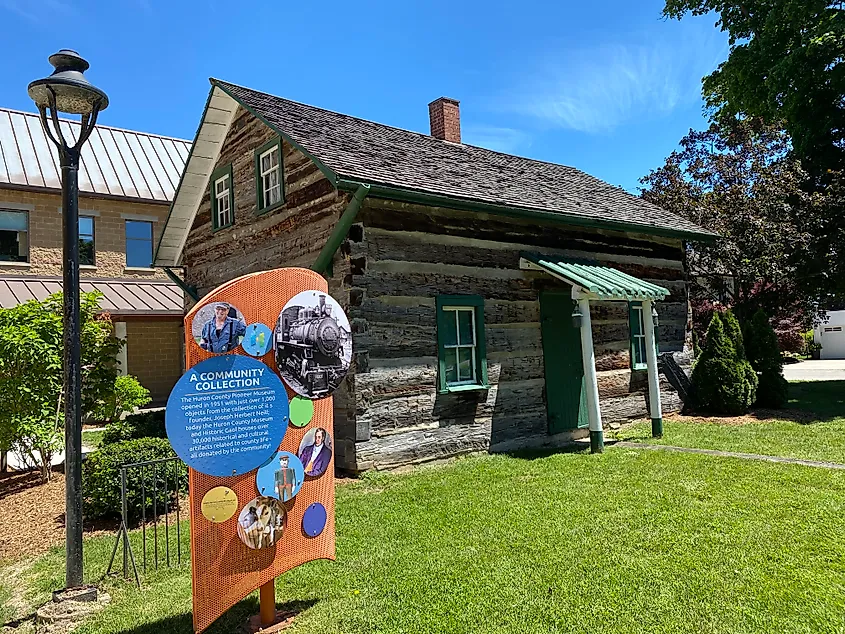 A wooden pioneer cabin preserved on the lawn outside of a museum. 