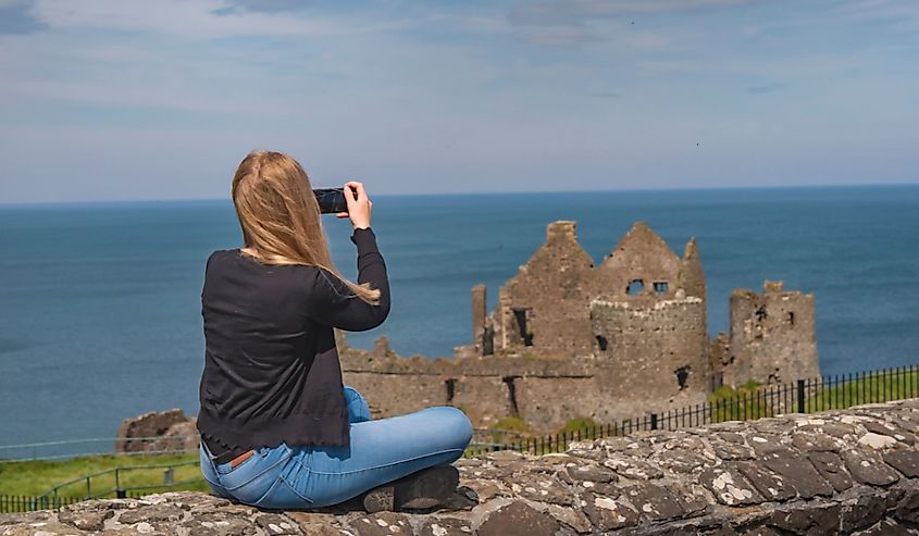 Young woman takes photo of castle in Northern Ireland. 