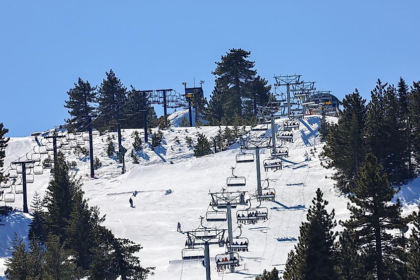 Snowed mountain slopes with people snowboarding and on the chairlifts at Snow Valley Ski Resort in Running Springs California.